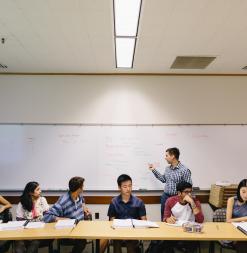 An instructor speaks at the whiteboard as participants look on.